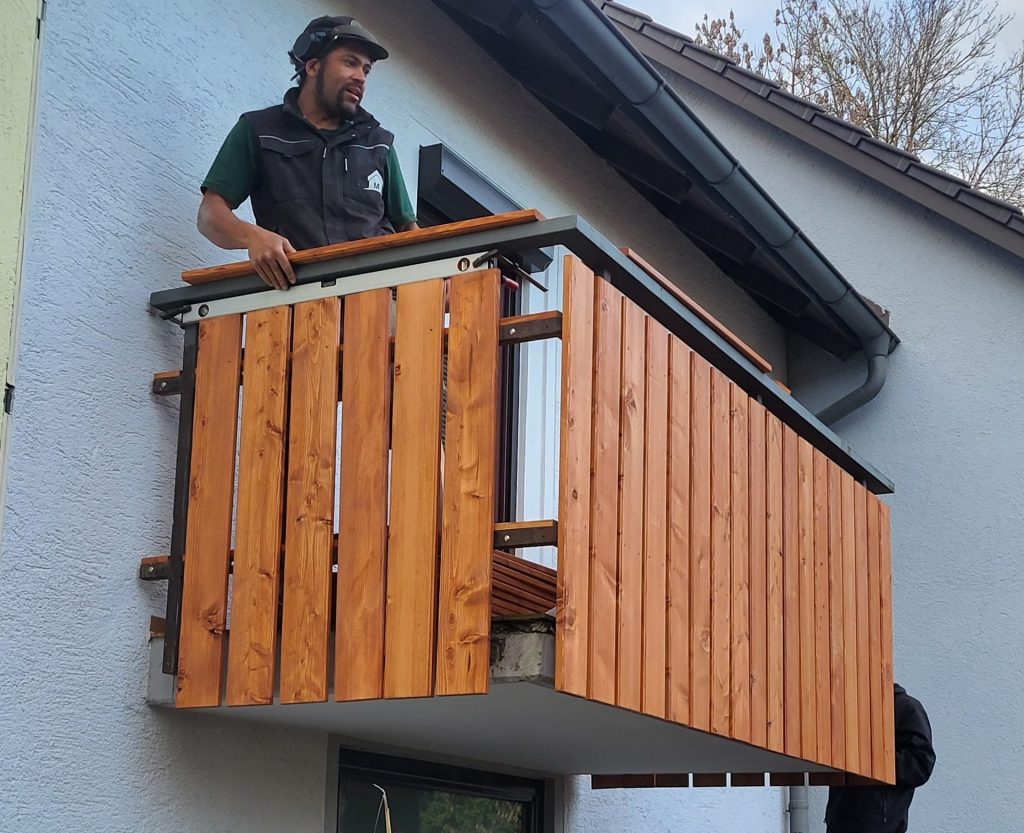 Handwerker vom Hausmeisterservice Max bei der Montage einer neuen Balkonverkleidung aus Holz an einem Wohnhaus in München Obermenzing.